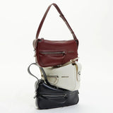 Stacked Amazing Song handbags in burgundy, white, and black with zipper details
