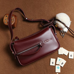 Amazing Song maroon leather shoulder bag with zipper, pom pom charm, and numbered tiles on brown background