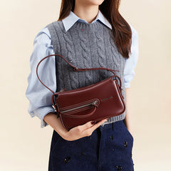 Woman holding a burgundy leather handbag, wearing a gray cable knit vest and blue shirt
