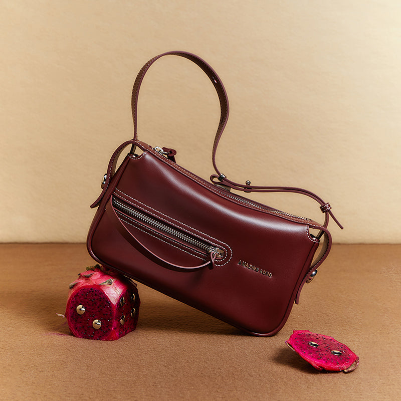 Amazing Song burgundy leather handbag with zipper detail, styled with dragon fruit on beige background