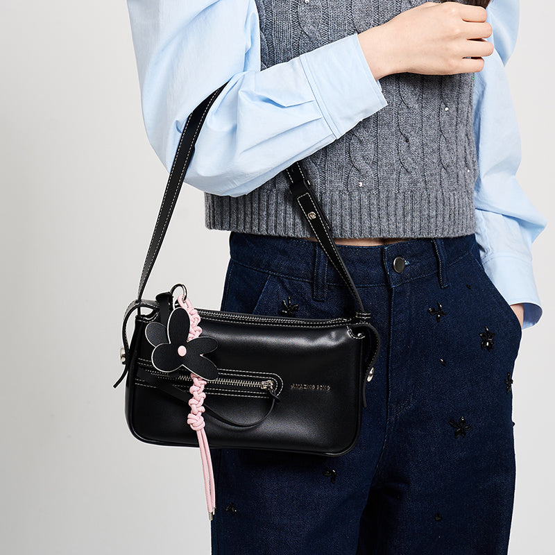Woman wearing grey sweater and blue shirt with black Amazing Song crossbody bag and flower keychain