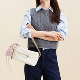 Woman in a grey knit vest and blue shirt holding a white Amazing Song handbag