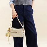 Woman holding cream Amazing Song handbag, wearing navy embroidered pants and grey sweater