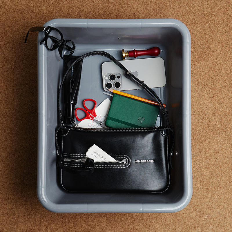 Amazing Song black handbag in tray with glasses, phone, notebook, and accessories