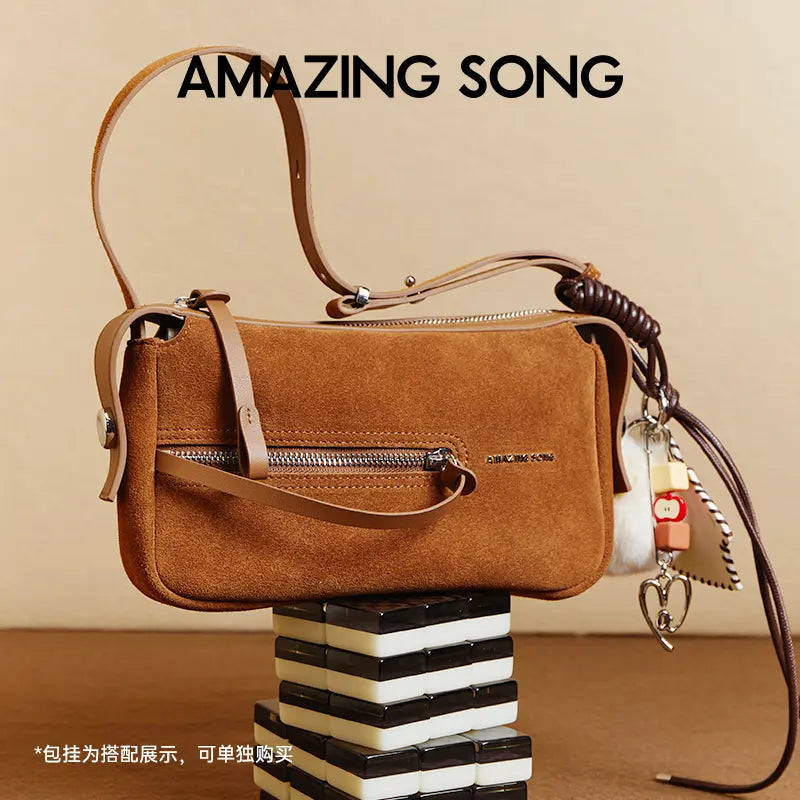 Amazing Song brown suede handbag with zipper, keychain charms, and leather strap on display.