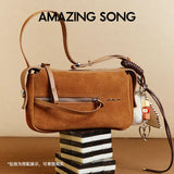Amazing Song brown suede handbag with zipper, keychain charms, and leather strap on display.