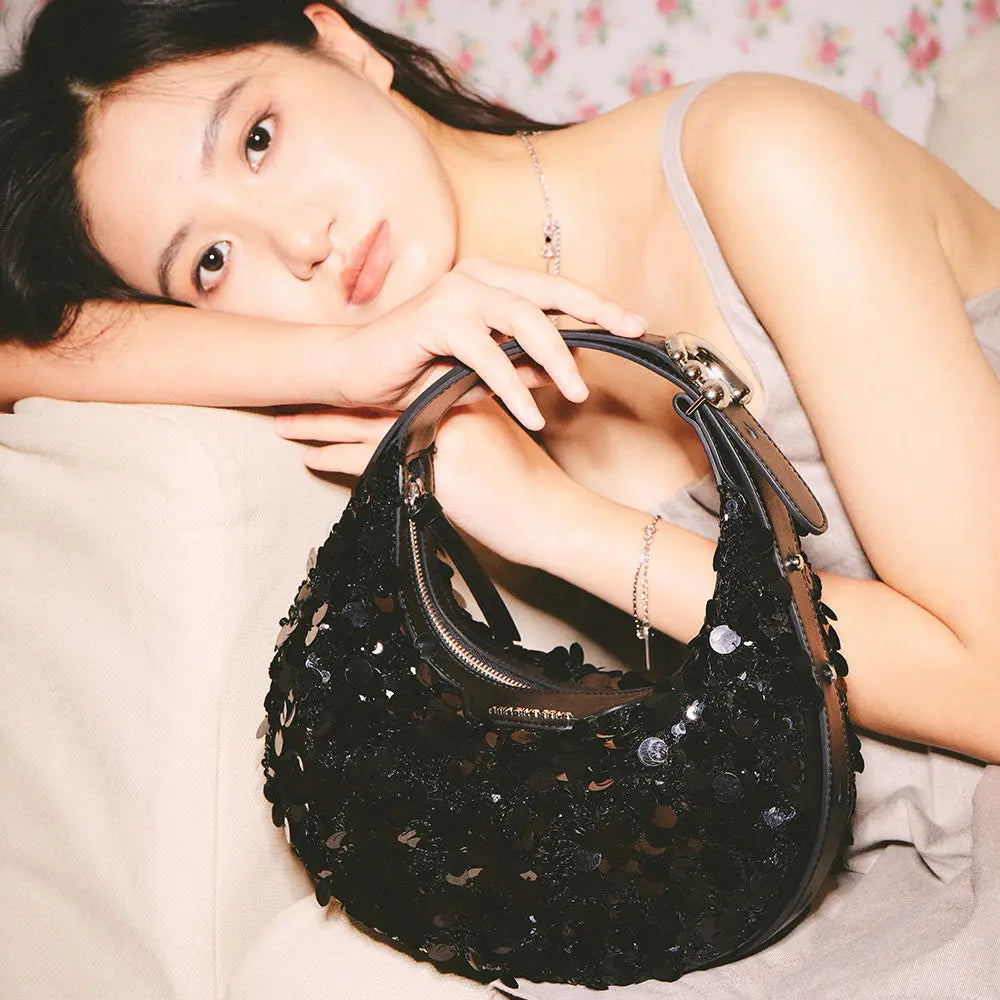 Woman in gray dress leaning on a beige sofa holding a black sequin handbag, Amazing Song