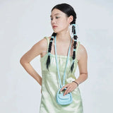 Woman in pastel green satin dress with braids and blue mini bag, Amazing Song fashion