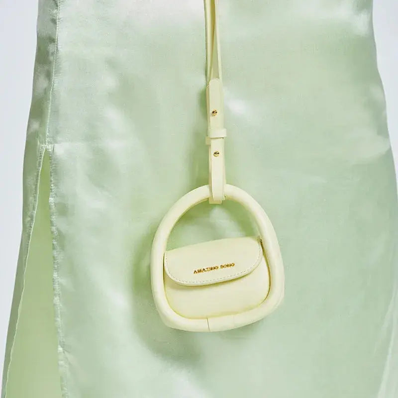 Pastel yellow mini handbag with Amazing Song logo, hanging on a light green satin dress