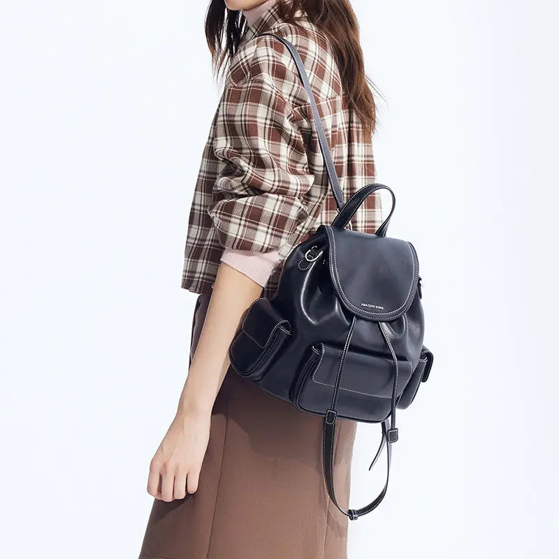 Woman carrying black leather backpack, brown plaid shirt, Amazing Song style fashion