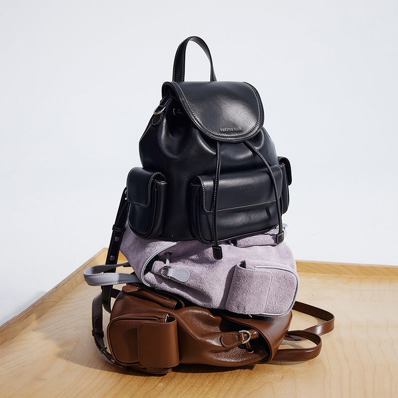 Stack of stylish leather and suede backpacks in black, lilac, and brown on a wooden table