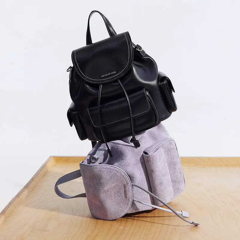 Amazing Song black leather and lavender suede backpacks stacked on wooden surface