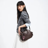 Woman in grey sweater holding dark brown handbag with pink heart charm, Amazing Song style