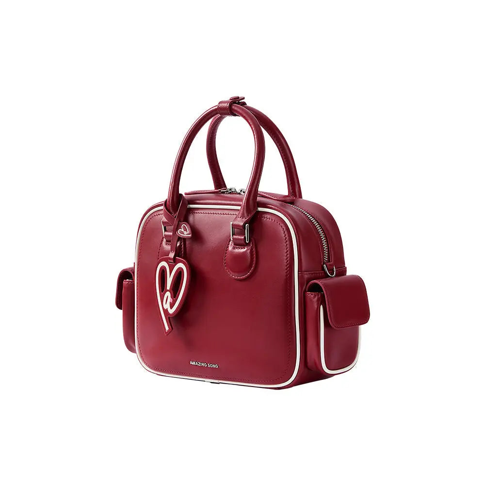 Red Amazing Song handbag with heart-shaped charm, top handles, and white trim on white background