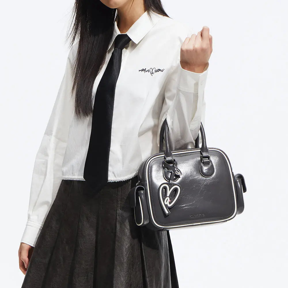 Woman in white shirt and tie holding a black Amazing Song handbag with heart charm
