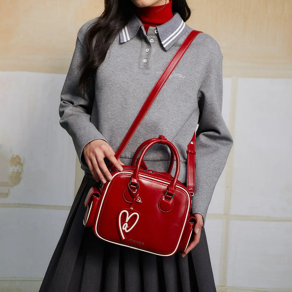 Woman in grey top with pleated skirt carrying a stylish red Amazing Song handbag.