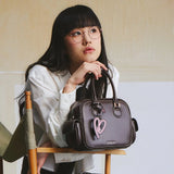 Woman with glasses in white shirt holding brown Amazing Song handbag with pink heart charm