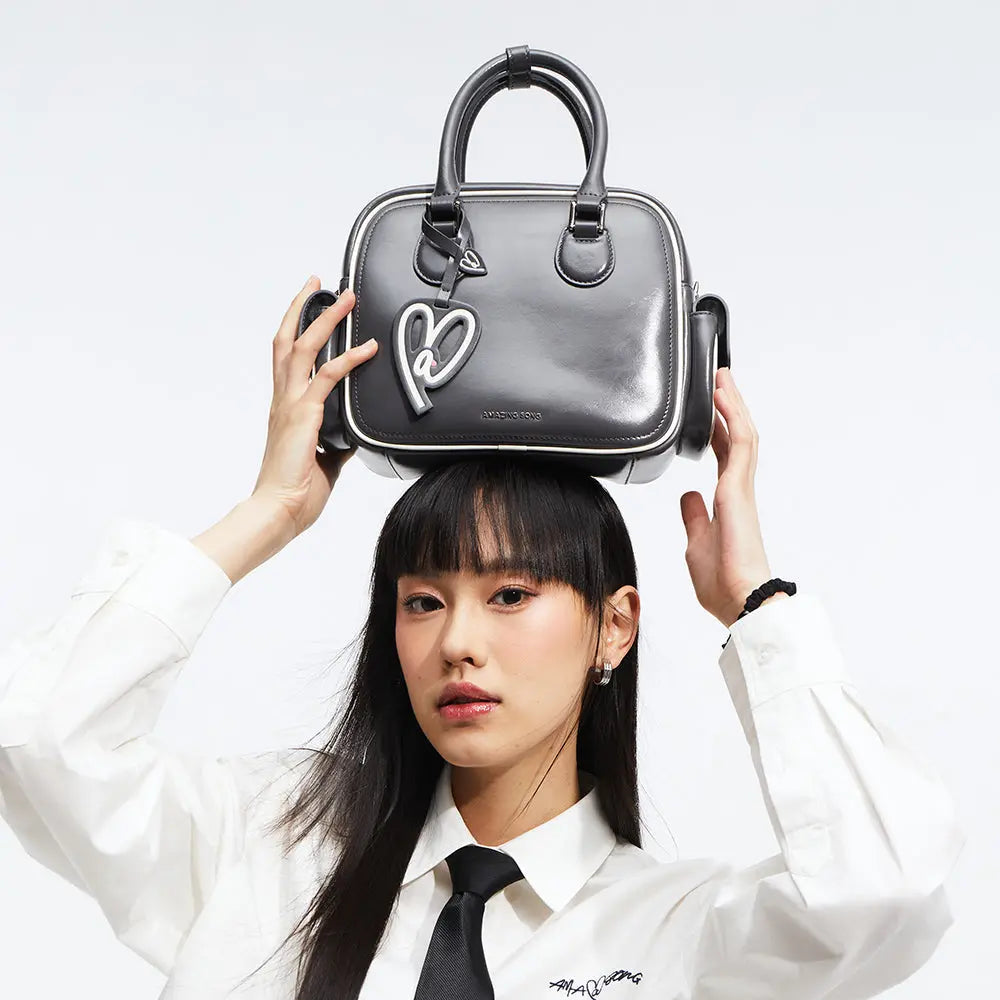 Woman in white shirt with black tie holding black Amazing Song handbag on her head