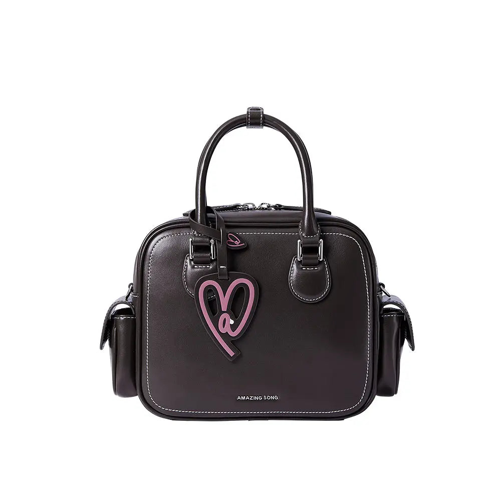 Amazing Song black leather handbag with pink heart accent, white stitching, and side pockets