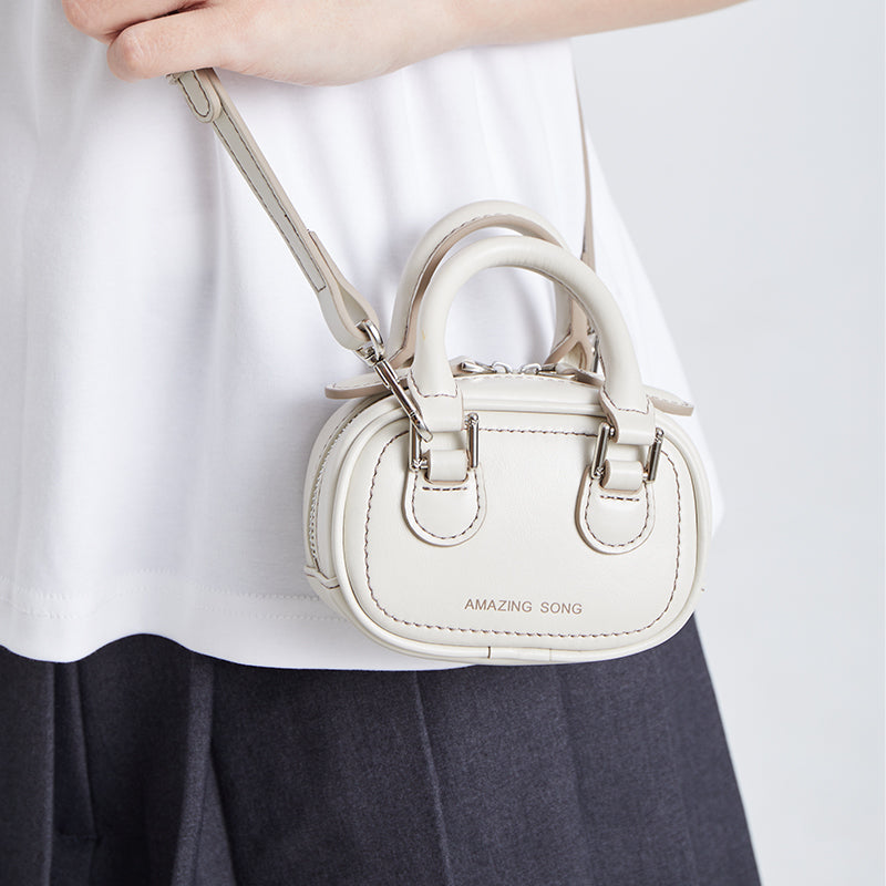 Woman wearing a small white Amazing Song handbag with top handles and crossbody strap.