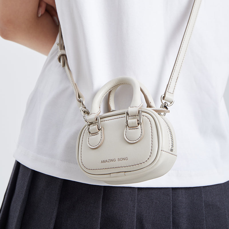 Small white crossbody bag with Amazing Song logo, worn over a white shirt and dark skirt
