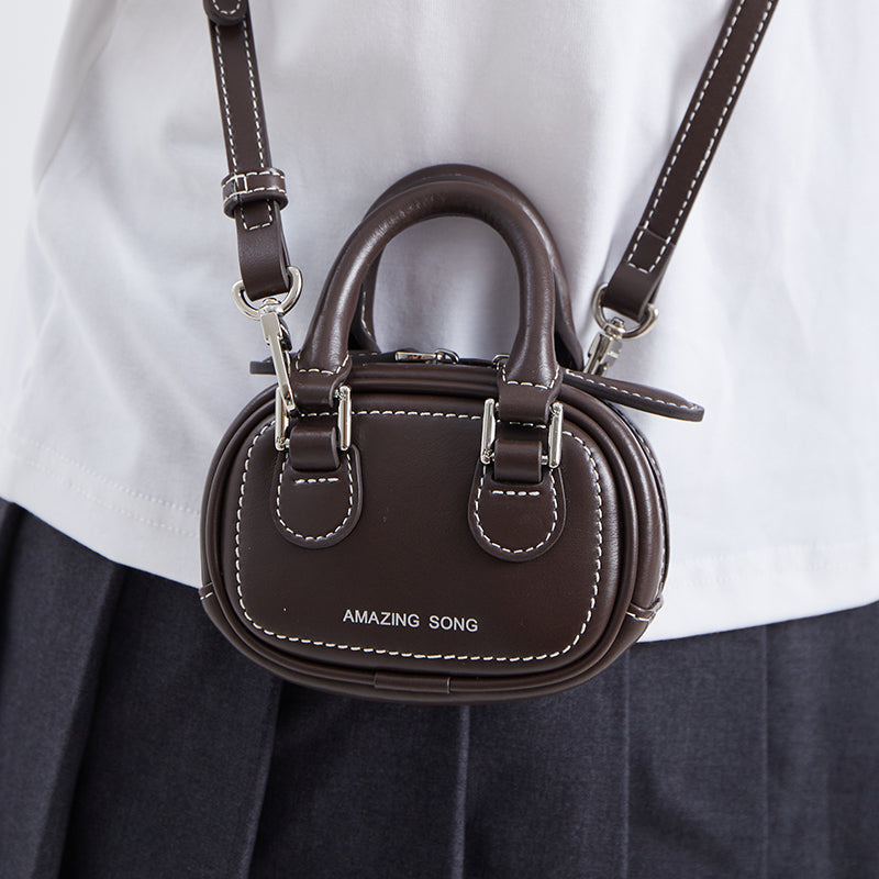 Brown mini crossbody bag with white stitching and 'AMAZING SONG' logo, worn on shoulder