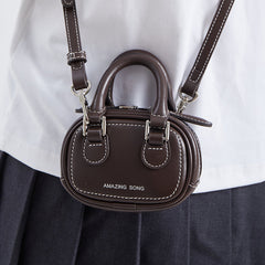 Brown mini crossbody bag with white stitching and 'AMAZING SONG' logo, worn on shoulder
