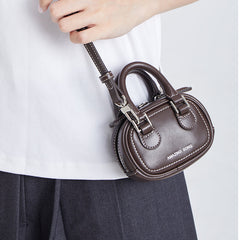 Hand holding small brown leather handbag with Amazing Song logo, white shirt background