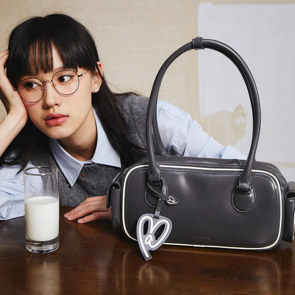 Woman with glasses beside a black Amazing Song handbag and glass of milk on table