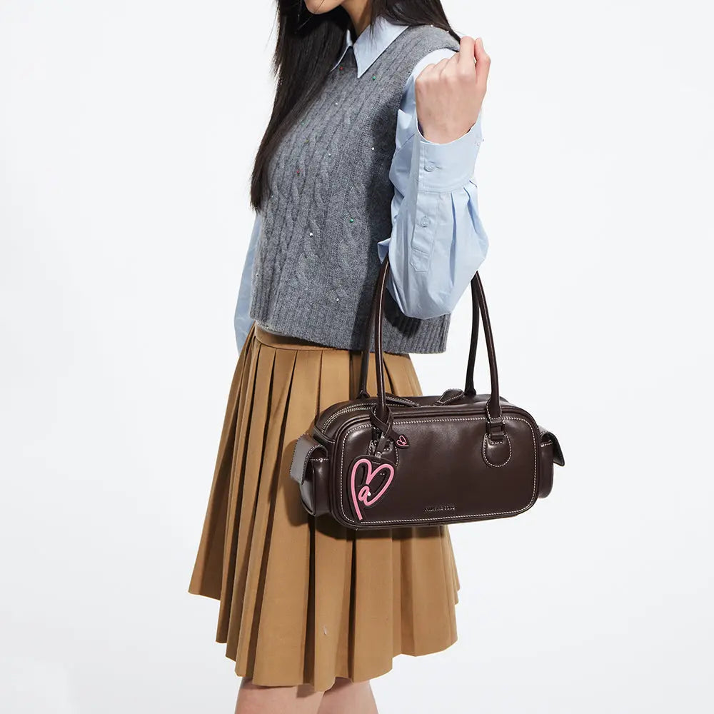 Woman holding dark brown handbag with pink heart tag, pleated skirt, Amazing Song style