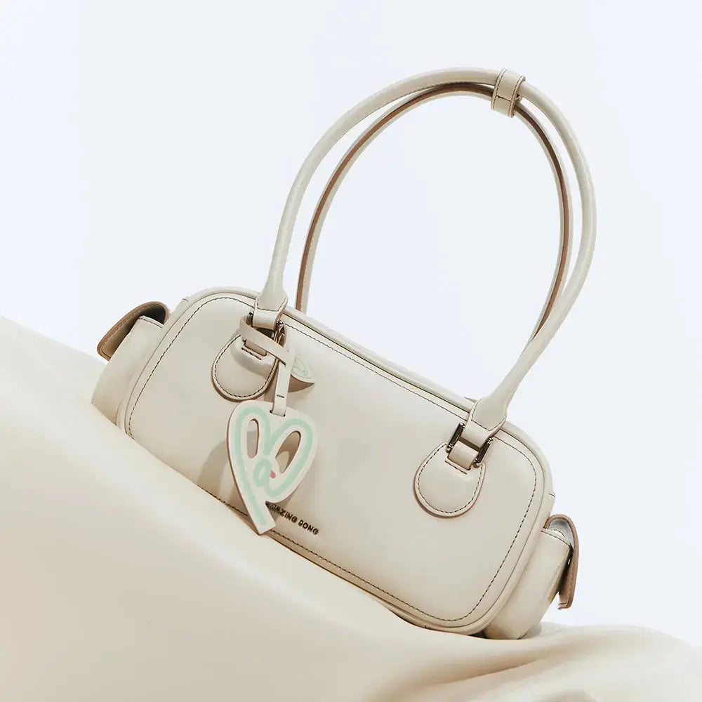 Beige Amazing Song handbag with dual handles and heart charm on a matching background