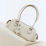 Beige Amazing Song handbag with dual handles and heart charm on a matching background