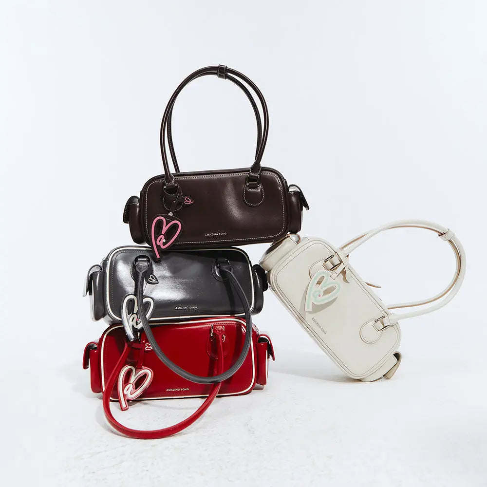 Stack of Amazing Song handbags in brown, black, red, and cream with heart keychains