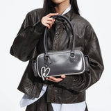 Woman in dark leather jacket holding glossy gray Amazing Song handbag with heart charm