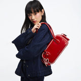 Woman in dark denim jacket posing with a red Amazing Song shoulder bag and heart keychain