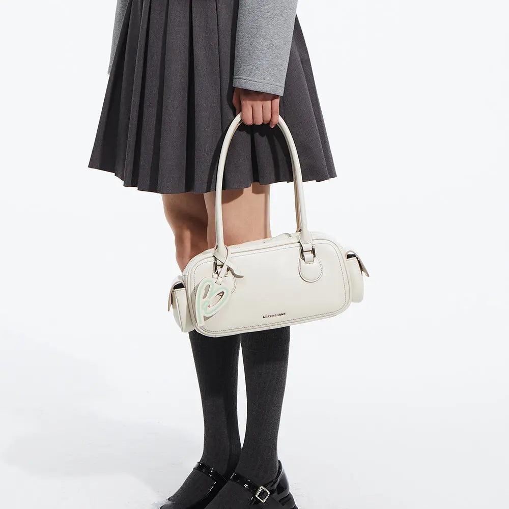 Woman in pleated skirt holding Amazing Song white handbag with heart charm
