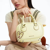 Woman holding pastel yellow Amazing Song handbag with heart-shaped tag, modern fashion