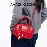 Woman wearing a red Amazing Song crossbody bag with heart tag, gray sweater, and jeans