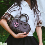 Woman holding brown Amazing Song handbag with pink heart charm outdoors