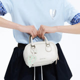 Woman holding white Amazing Song handbag with logo tag, wearing light blue shirt and navy skirt