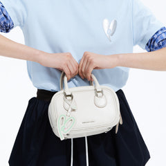 Woman holding white Amazing Song handbag with logo tag, wearing light blue shirt and navy skirt