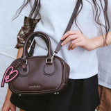 Amazing Song brown handbag with pink heart keychain, worn crossbody by woman in casual outfit