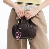 Woman holding dark brown Amazing Song handbag with pink heart charm, neutral fashion outfit