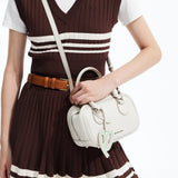 Woman in brown dress holding a white Amazing Song handbag with heart keychain