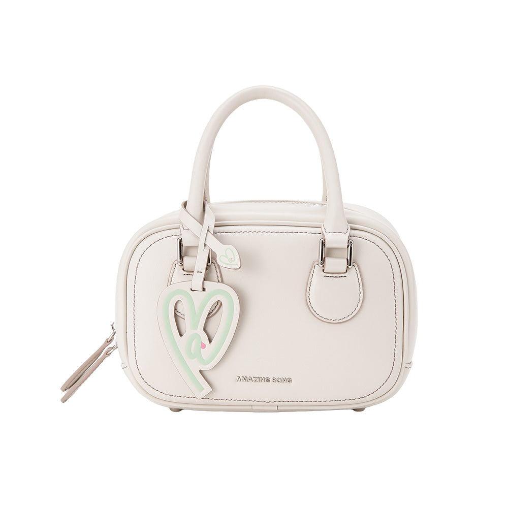 Amazing Song beige handbag with heart charm and twin handles on white background