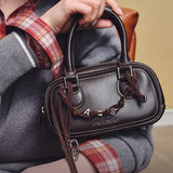 Woman holding brown Amazing Song leather handbag with decorative charms, close-up