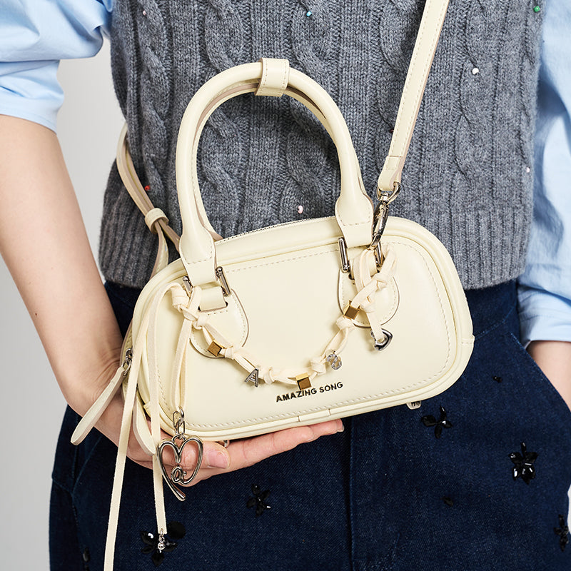 Amazing Song cream handbag with heart charm, crossbody style, held by person in grey vest