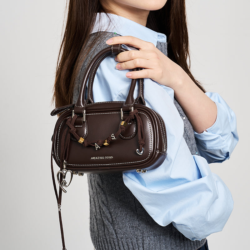 Woman holding brown Amazing Song handbag with silver accents and letter charms