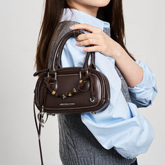 Woman holding brown Amazing Song handbag with silver accents and letter charms