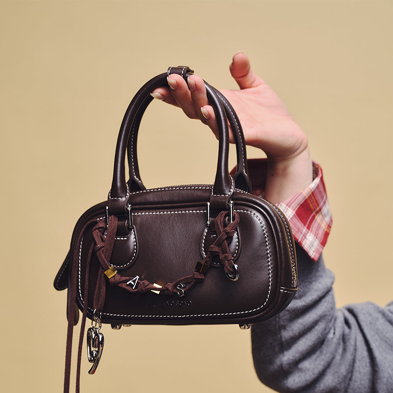 Hand holding dark brown leather mini handbag with double handles and decorative charms